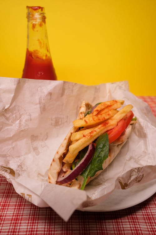 Free High angle of gyro with french fries and fresh vegetables in parchment paper on table with ketchup bottle against yellow background Stock Photo